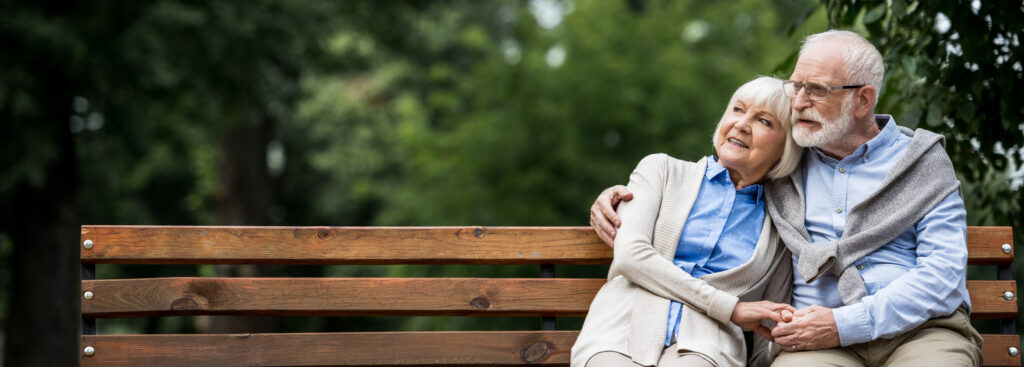 smiling senior couple embracing while sitting on wooden bench in park