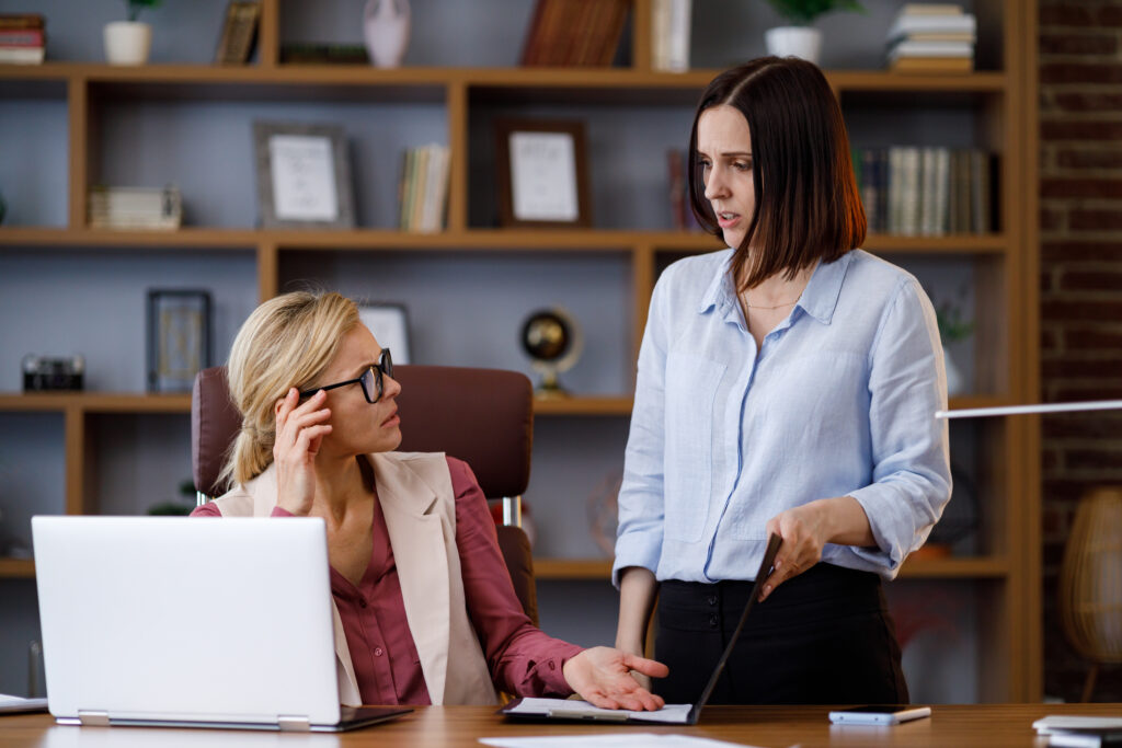 Angry female boss scolding sad and scared office worker. Demanding manager leader is annoyed at laziness and mistakes in paperwork of employee