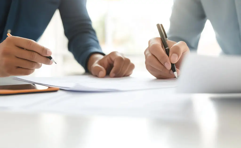 Two people writing and reviewing documents together at a desk