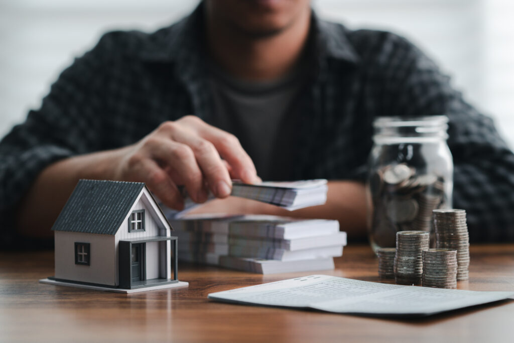 Man organizes cash with coins, a contract, and a miniature house, symbolizing financial management, investment, and real estate planning. Savings Plan, Down Payment, Mortgage, Home Equity
